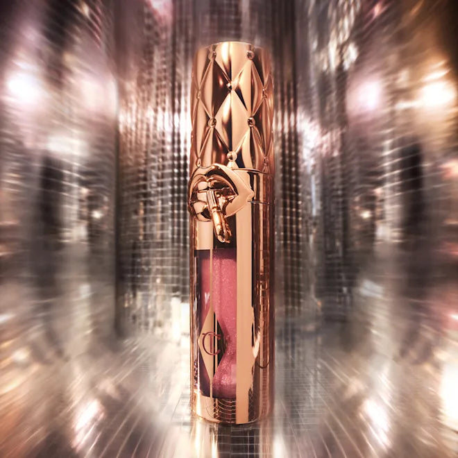 Charlotte Tilbury Big Lip Plumpgasm lip gloss in metallic rose gold tube with shimmering pink shade, photographed against a reflective background.