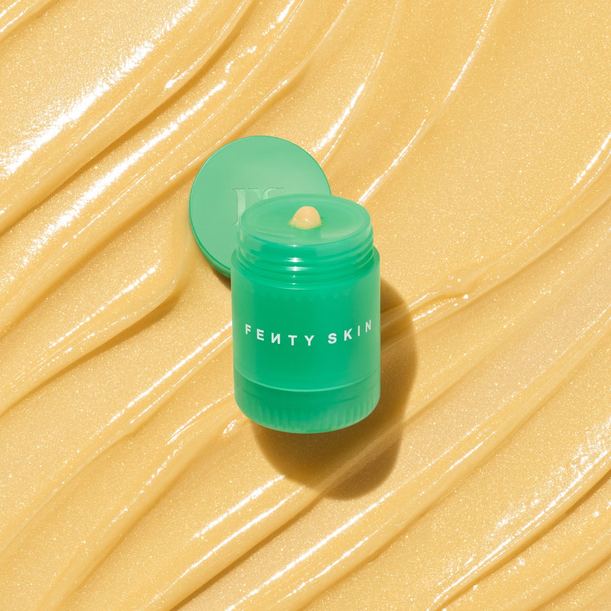 Green Fenty Skin container on a beige textured background