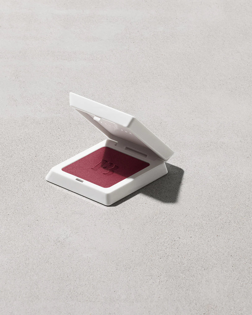 Compact powder case with red powder on a light gray background