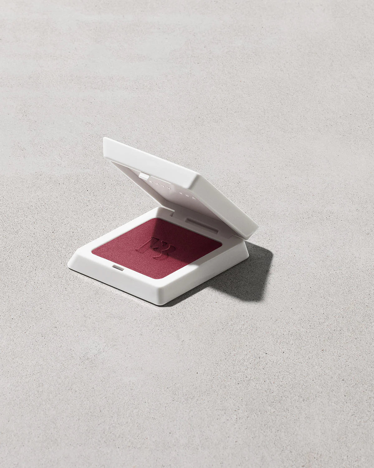 Compact powder case with red powder on a light gray background