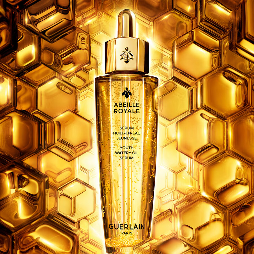 Guerlain Abeille Royale Youth Watery Oil Serum bottle displayed upright against a bright golden honeycomb background with visible suspended microbeads